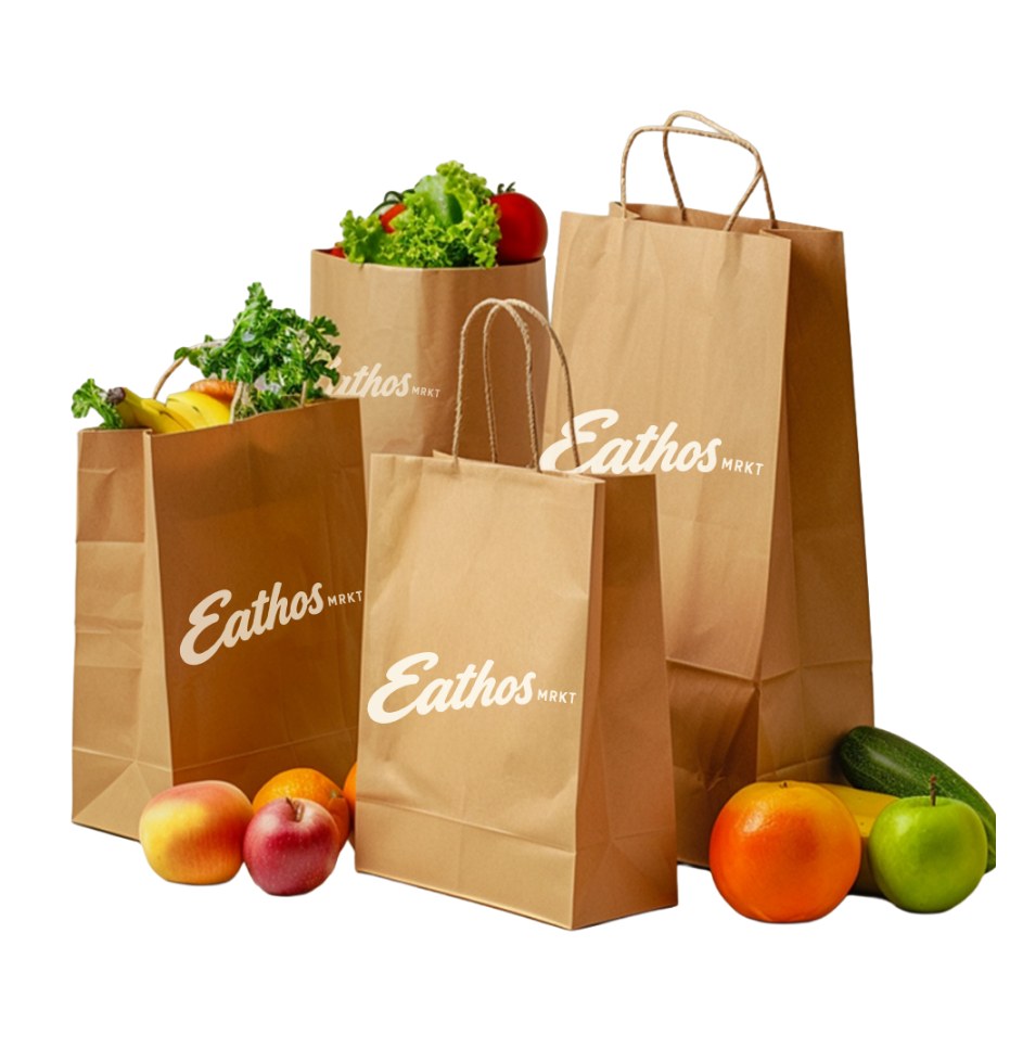 Four Eathos Mrkt paper grocery bags filled with produce, with apples, oranges and a zucchini beside them