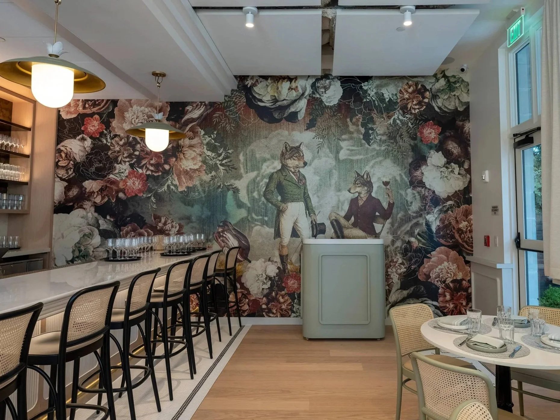 Inside Lupo Notte: bar seating and a set table in front of the floral mural with two dressed wolves