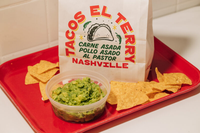 A Tacos El Terry takeout bag on a red tray with tortilla chips and guacamole